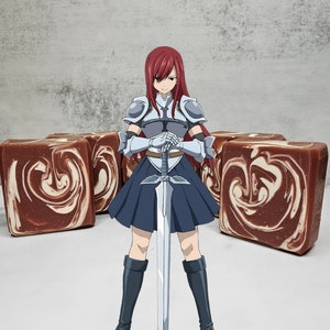 Puede incluir: Un personaje femenino de anime con cabello rojo largo, vistiendo una armadura plateada y una falda azul, sostiene una espada plateada frente a ella. Está de pie frente a cuatro barras de jabón marrones y blancas con un patrón de espiral.