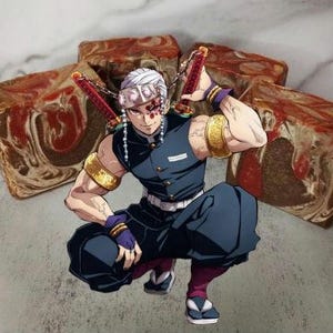 Puede incluir: Un personaje del anime Demon Slayer, con un atuendo negro y azul con una máscara estampada en blanco y rojo, sostiene una espada y se encuentra frente a una pila de barras de jabón con patrones de remolino marrón y rojo.