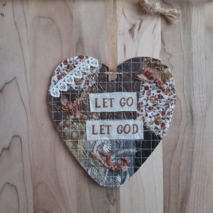 May include: Heart-shaped wall hanging with the text "LET GO LET GOD". The patchwork design features floral and patterned fabric in shades of brown, cream, and red, accented with white lace and stitched details. A jute string is attached for hanging.