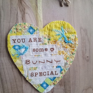 May include: A yellow heart-shaped fabric ornament with the text "You are some bunny special" in brown lettering.