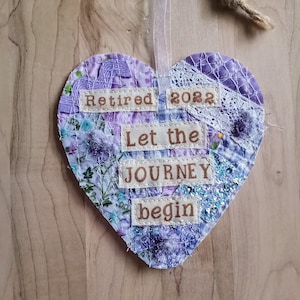 May include: Purple heart-shaped ornament with a patchwork design and the text "Retired 2022 Let the Journey begin".