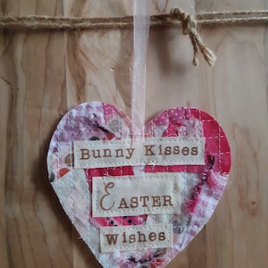 May include: A pink and white patchwork heart-shaped ornament with the text "Bunny Kisses & Easter Wishes".