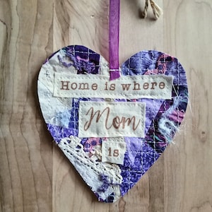 May include: Purple and white fabric heart with the text "Home is where Mom is" and the number "18" on it. The heart is hanging from a purple ribbon.