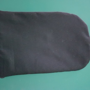 Puede incluir: Una bolsa negra rectangular con esquinas redondeadas. La bolsa está hecha de una tela oscura y suave y está colocada sobre un fondo verde. La bolsa parece estar vacía.
