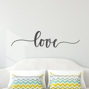May include: A white bed with a yellow bedspread and two pillows with a chevron pattern. The headboard has a black vinyl decal that says "love" above it.