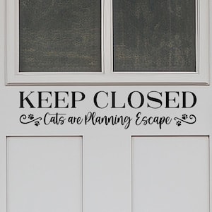 May include: A white door with a black vinyl decal that reads "Keep Closed Cats are Planning Escape".