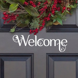 May include: A white vinyl decal with the word "Welcome" in a decorative script font on a dark gray door. A red and green holiday wreath is above the decal.