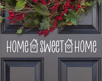 May include: A gray front door with a white wreath and the text "Home Sweet Home" with a house and heart symbol on each side of the word "Sweet".