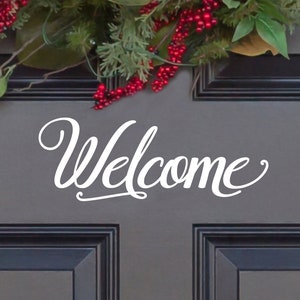 May include: A gray front door with a black frame and a white cursive "Welcome" sign. A Christmas wreath with red berries and green leaves hangs above the sign.