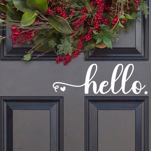 May include: A dark gray front door with a white vinyl decal that says "hello" with two small hearts. A Christmas wreath with red berries and green leaves hangs above the door.