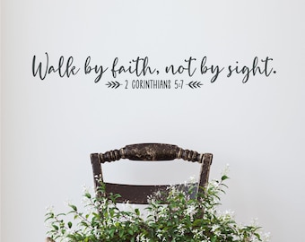 Puede incluir: Un vinilo decorativo de pared en color gris oscuro con el texto en cursiva e imprenta Walk by faith, not by sight. 2 CORINTHIANS 5:7 y pequeños iconos de hojas decorativas a ambos lados de la referencia bíblica, sobre una silla de madera.
