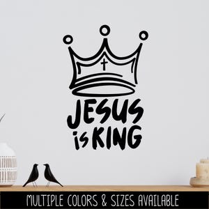 May include: Black graphic of a crown with a cross and the text "JESUS is KING" on a white background. The bottom of the image has the text "MULTIPLE COLORS & SIZES AVAILABLE".