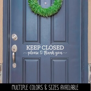 May include: A dark blue door featuring a white vinyl decal that reads KEEP CLOSED please & thank you in a combination of block and script lettering. A green circular wreath is mounted at the top center of the door above the text.