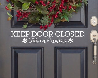 Peut inclure: Autocollant en vinyle blanc avec le texte "KEEP DOOR CLOSED Cats on Premises" avec des empreintes de pattes de chaque côté du texte. L'autocollant est sur une porte gris foncé avec une couronne de Noël au-dessus.