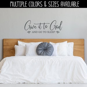 May include: A white bed with a wooden headboard and white bedding. The wall behind the bed has a gray vinyl decal that reads "Give it to God and go to sleep".