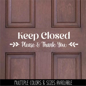 May include: White vinyl decal with the text "Keep Closed Please & Thank You" on a brown wooden door. The decal has a simple floral design on either side of the text.