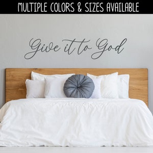 May include: A white bed with a wooden headboard and white bedding. A gray round pillow is on the bed. The wall behind the bed has a gray vinyl decal that says "Give it to God".