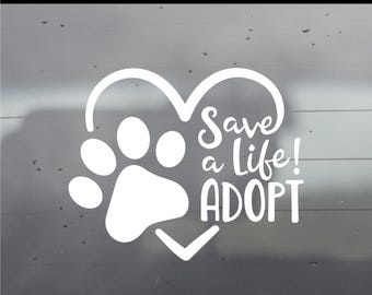 May include: A white vinyl decal featuring a paw print integrated into a heart shape with the text Save a Life! ADOPT. The top of the image includes the text MULTIPLE COLORS & SIZES AVAILABLE. The design is displayed against a gray background.