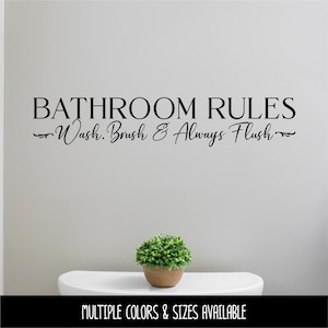 May include: A bathroom wall decal with the words "Bathroom Rules: Wash, Brush & Always Flush" in black script. A small potted plant sits on a white toilet. The bottom of the image reads "MULTIPLE COLORS & SIZES AVAILABLE."