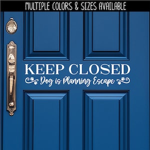May include: A blue door with a gold handle and a white sign that reads "KEEP CLOSED Dog is Planning Escape". The text "MULTIPLE COLORS & SIZES AVAILABLE" is at the top. The door has a paneled design.