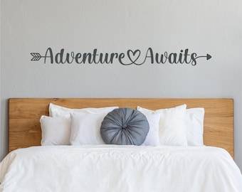 Peut inclure: Un autocollant mural gris avec les mots "Adventure Awaits" en écriture cursive, avec une flèche et un cœur. L'autocollant est au-dessus d'une tête de lit en bois et d'une literie blanche. Le texte "MULTIPLE COLORS & SIZES AVAILABLE" est en haut.