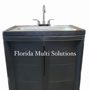 May include: A dark gray outdoor sink with a stainless steel basin and a chrome faucet. The cabinet doors have the text "Florida Multi Solutions" printed on them. The sink is designed for outdoor use.