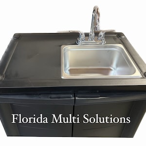 May include: Black portable sink with a stainless steel sink basin and a chrome faucet. The sink has two doors with the text "Florida Multi Solutions" on the front.