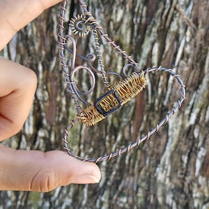 May include: A wire-wrapped ornament shaped like a witch hat, constructed from dark copper-toned wire with a coiled gold-toned wire band and a small black rectangular buckle detail, featuring intricate wire loops and swirls throughout the structure.