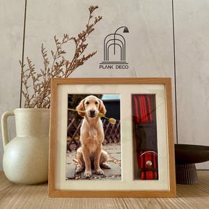 Może przedstawiać: Drewniana ramka na zdjęcia ze zdjęciem złotego retrievera trzymającego kwiat w pysku. Ramka ma oddzielny przedział na czerwoną i czarną obrożę dla psa.