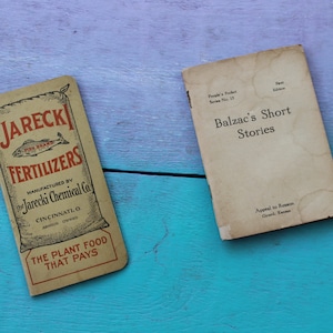May include: Two vintage books on a blue and purple wooden surface. One book is titled "Balzac's Short Stories" and the other is a fertilizer advertisement with the text "Jarecki Fertilizers".