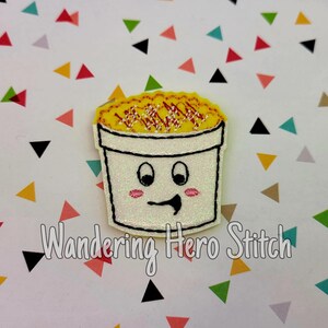以下が含まれることがあります： 笑顔のラーメン丼の形をした白いキラキラワッペン。ラーメンは黄色い麺と茶色のトッピングです。「Wandering Hero Stitch」の文字が下にあります。