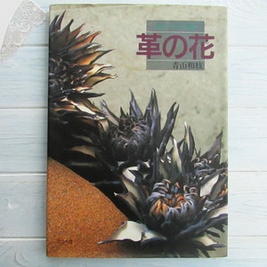 May include: A book cover with a close-up image of a dark, spiky flower. The title of the book is "幸の花" in Japanese characters, which translates to "Flower of Happiness". The author's name is "佐山和枝" in Japanese characters.