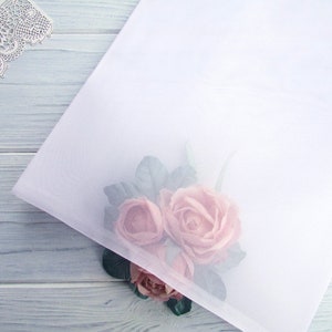 Può includere: Un foglio di tessuto bianco trasparente con un bouquet di rose rosa su uno sfondo di legno blu chiaro.