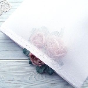 Könnte beinhalten: Weißer, durchsichtiger Stoff mit einem zarten Blumendesign mit zwei rosa Rosen. Der Stoff hat einen dezenten Glanz und eine weiche, fließende Textur.