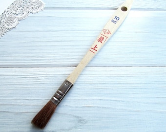 May include: A wooden paintbrush with a brown bristle brush head and a white handle. The handle has blue and red markings with the text "10 mm" and "最高" in Japanese characters.