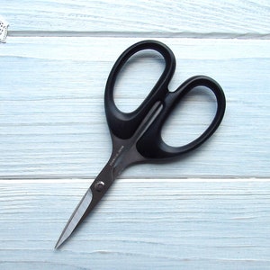 Może przedstawiać: Nożyczki z czarnym uchwytem i srebrnymi ostrzami na jasnoniebieskim drewnianym tle.