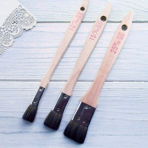 May include: Three wooden paint brushes with black bristles and red labels. The labels read "10 mm", "15 mm", and "25 mm".