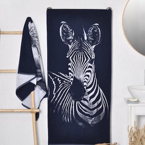 May include: A navy blue bath towel with a white zebra print. The towel is hanging on a wooden towel rack.