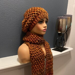 May include: A brown and orange crocheted beanie and matching scarf. The beanie has a textured, puffy design. The scarf is long and narrow.