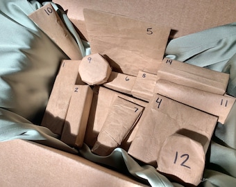 May include: A selection of numbered brown paper packages, of various sizes and shapes, presented in a box lined with sage green fabric. The arrangement suggests a gift set or advent calendar, ready to be opened.