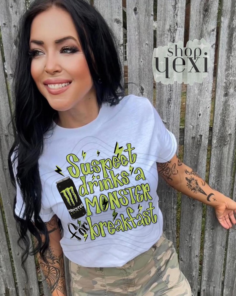 May include: White t-shirt with the text "Suspect drinks a MONSTER for breakfast" in green and black. The shirt features a graphic of a Monster energy drink can. The shirt is worn by a person.