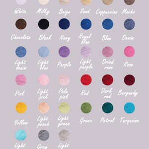 Op de afbeelding: Een kleurenkaart met een verscheidenheid aan garenkleuren, waaronder wit, zwart, blauw, roze en groen. Elke kleur wordt weergegeven in een kleine cirkel met de kleurnaam in witte letters. De achtergrond is lichtpaars.
