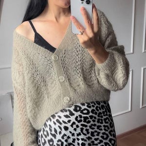 May include: A woman wearing a black beret, gold earrings, and a light beige cardigan with large buttons. She is also wearing a black top and a leopard print skirt. The image includes the text "color 64407 M-L READY TO SHIP!"