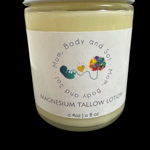 May include: A white jar with a yellow label that reads "Mom, Body and Sol. Mom, Sol, Body and" with a colourful graphic of a tree and a heart. The label also reads "Magnesium Tallow Lotion" and "o 4oz | o 8 oz".