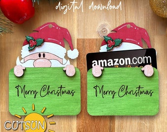 May include: Two green wooden gift card holders featuring a Santa Claus design. The holder on the left has the text "Merry Christmas" and the holder on the right has the text "amazon.com" and "Merry Christmas".
