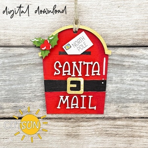 May include: A red wooden Santa mailbox ornament with gold trim and a black belt design. The words "SANTA MAIL" are in white, with a tag that says "NORTH POLE". The ornament has a holly and berry accent and is labeled "digital download".