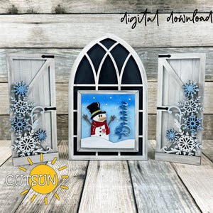 May include: A winter-themed decorative set featuring a central arched window with a snowman scene, flanked by two white wooden door panels adorned with snowflake accents. The set is painted in white and blue, with the text "digital download" visible.
