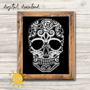 May include: A black and white sugar skull with intricate floral designs. The skull is framed in a brown wood frame.