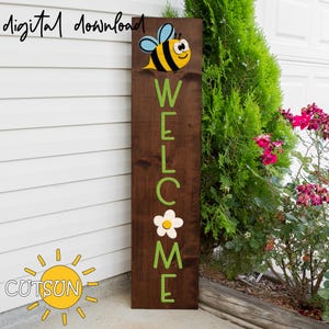 May include: A wooden welcome sign with the word "WELCOME" spelled out in green letters. A yellow and black bee with white eyes is above the word "WELCOME". A white flower with a yellow center is below the word "WELCOME".