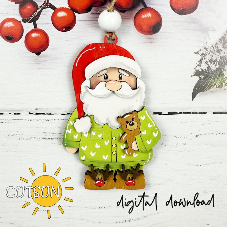 May include: A wooden Christmas ornament in the shape of Santa Claus wearing green pajamas with white hearts and reindeer slippers. Santa holds a teddy bear. The ornament has a red hat and white beard. The text "digital download" is visible.